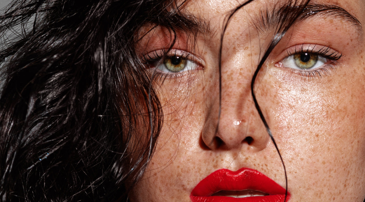 Brow Bandit Beauty closeup of a freckled woman's black hair glossy eyebrows green eyes and dark lips
